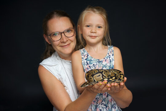  Young girl with mother holdind pet snake in her hands.