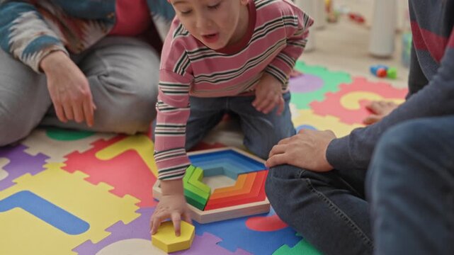 Boy playing with rainbow blocks while men clap hands in a building play area; joyful family bonding together.