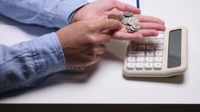Person's hands holding and counting coins with a calculator nearby, planning expenses, managing personal finance, and tracking saving goals for future investments