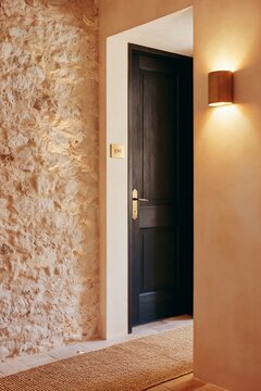 Boutique hotel hallway featuring rough stone walls, a dark wooden door, and warm lighting, creating a cozy and inviting atmosphere for guests