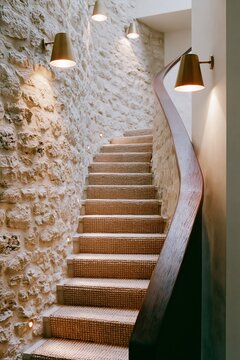 Boutique hotel stairwell featuring rough limestone walls, wooden handrail, and warm lighting illuminating the steps, creating an inviting atmosphere for guests
