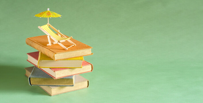 stack of books with deckchair and sun umbrella, spring and summer holiday read. Vacation summer holidays,travel, inspiration,relaxation with books,reading and literature concept.
