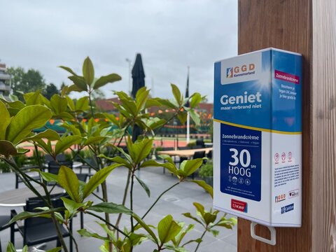 Haarlem, Netherlands, June 17, 2026: GGD sunscreen hangs in a tennis club, with blurred courts behind, offering free sun protection to prevent skin burns. Sports club health posters, skin cancer