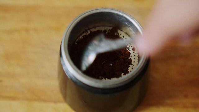 Putting ground coffee powder into a geyser moka pot filter funnel. Close up of someone filling an Italian espresso maker with aromatic dark ground coffee. Preparing ground coffee