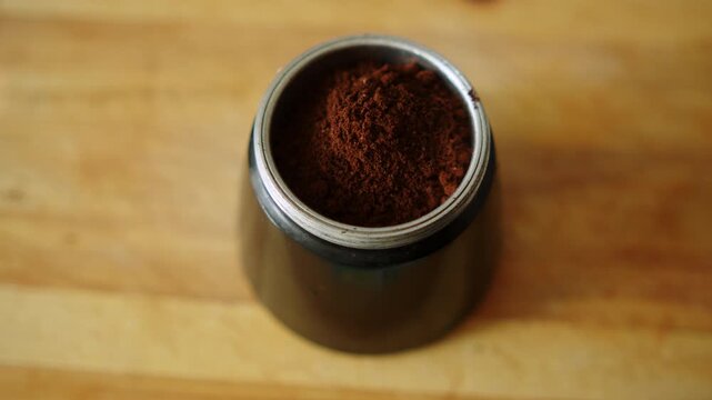 Close up of someone filling an Italian espresso maker with aromatic dark ground coffee. Putting ground coffee powder into a geyser moka pot filter funnel.  
