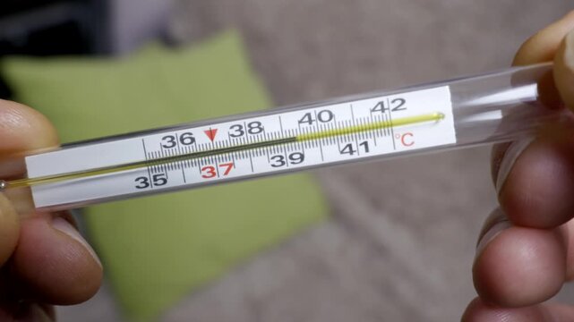 Person's hands hold a classic glass thermometer showing a reading of 39 degrees Celsius, indicating normal body temperature. Close-up shot with a shallow depth of field focuses on the Celsius scale.