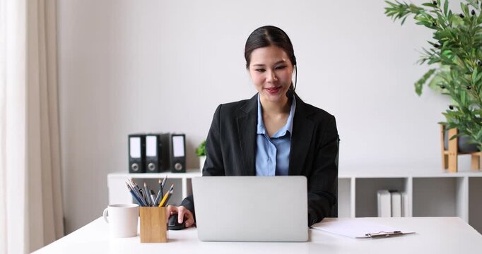 Asian businesswoman wearing a headset and smiling, providing online support in a call center, demonstrating excellent customer service and communication in an office setting