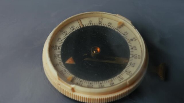 Vintage compass with a black dial is revealed through thick, billowing white smoke. Slow motion close up shot creates a mysterious atmosphere on a dark background.