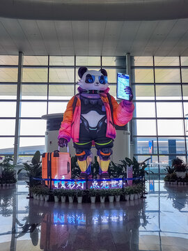 Chengdu, China - May 1, 2025: A large decorative panda mascot sculpture holding a smartphone and suitcase stands in the main terminal of Chengdu Tianfu International Airport.