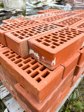 New red perforated brick pallets wrapped in plastic on a construction site.