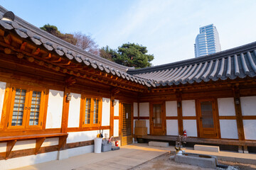 Fototapeta premium Traditional Korean hanok buildings with white walls, wooden frames, and dark tiled roofs in a sunlit courtyard