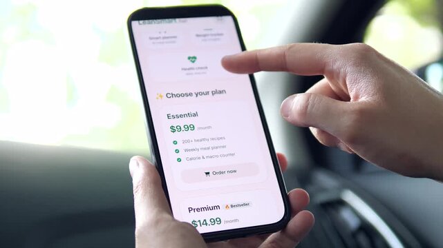 User exploring a weight loss app inside a car. Hand pointing at meal plans and premium subscription options. Perfect for fitness, diet coaching, and health tech stock video.