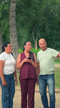 Parents and daughter deciding direction using smartphone map in park in vertical format