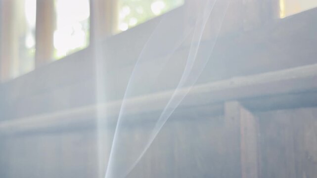 A thin trail of white smoke drifts upward in front of a rustic wooden window. The soft morning light creates a deeply nostalgic and lonely feeling. It feels quietly peaceful.