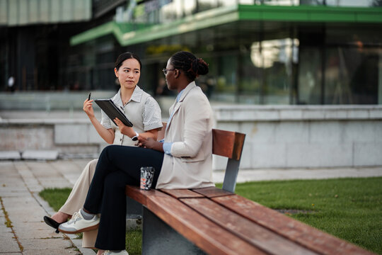 Diverse businesswomen discussing work outdoors using digital tablet