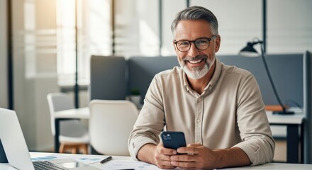 Obraz premium Confident Mature Businessman Smiling while Holding Smartphone in Modern Office Workspace