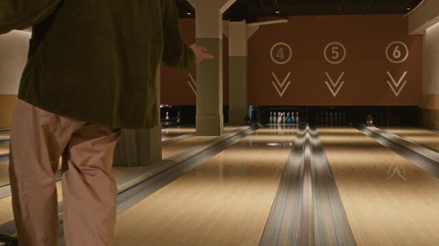 Caucasian young adult man throwing blue bowling ball on lane in bowling alley. Clip is ideal for recreational lifestyle commercials, entertainment promos, or team building advertisements