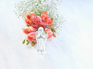 Obraz premium Beautiful praying angel figurine with bouquet of rose and gypsophila flowers on light abstract background. Religious church holiday. symbol of faith in God, pray, believe, christianity. flat lay