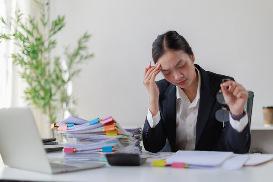Young Asian businesswoman sitting at her office desk. Holding her head with one hand due to a severe headache caused by stress and overwork