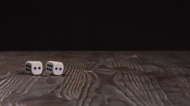 Close-up, side view, of two dice being thrown on a wooden table, both coming up the same