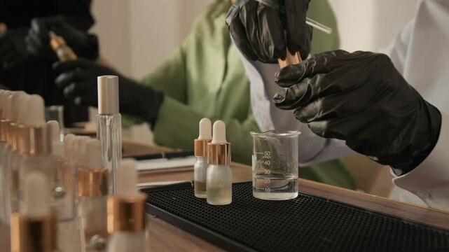 Hands in black gloves dripping essential oil from pipette into beaker during perfumery master class. Video is ideal for promoting cosmetics formulation workshops or DIY beauty product tutorials