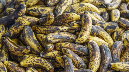 Pile of ripe, overripe bananas with dark spots and yellow skin, arranged closely together on a surface, showcasing their natural texture and color variations © Telly