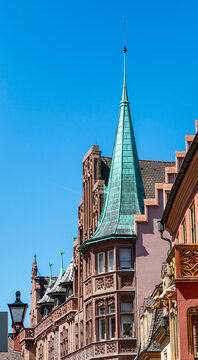 View of the ornate red sandstone facade and green copper spire of the Haus zum Walfisch against a clear blue sky in Freiburg im Breisgau, Baden-Wurttemberg, Germany.