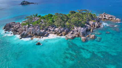 Stunning drone shot of Cocos Island, Seychelles, showing a luxury catamaran and boat anchored in clear turquoise water surrounded by granite rocks and coral reefs. © Nils