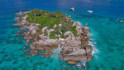 Stunning drone shot of Cocos Island, Seychelles, showing a luxury catamaran and boat anchored in clear turquoise water surrounded by granite rocks and coral reefs. © Nils