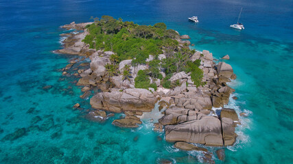 Stunning drone shot of Cocos Island, Seychelles, showing a luxury catamaran and boat anchored in clear turquoise water surrounded by granite rocks and coral reefs. © Nils