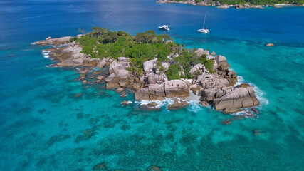 Stunning drone shot of Cocos Island, Seychelles, showing a luxury catamaran and boat anchored in clear turquoise water surrounded by granite rocks and coral reefs. © Nils