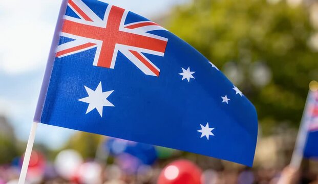 A small Australian flag waving proudly in a blurred outdoor crowd setting, symbolizing national identity and celebration.