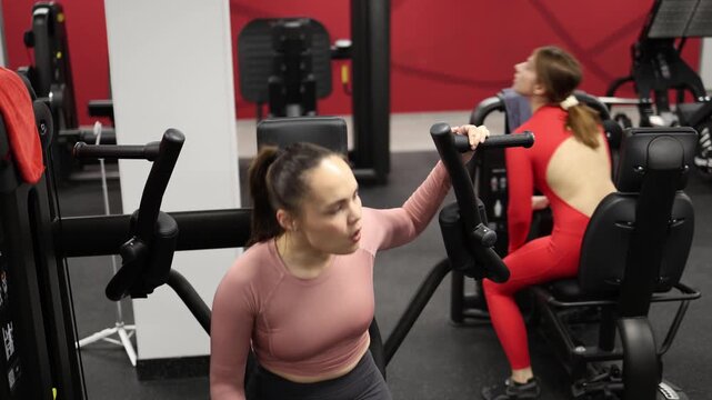 Two friends train side by side at gym taking turns on exercise machines supporting each other after each set and staying motivated throughout workout