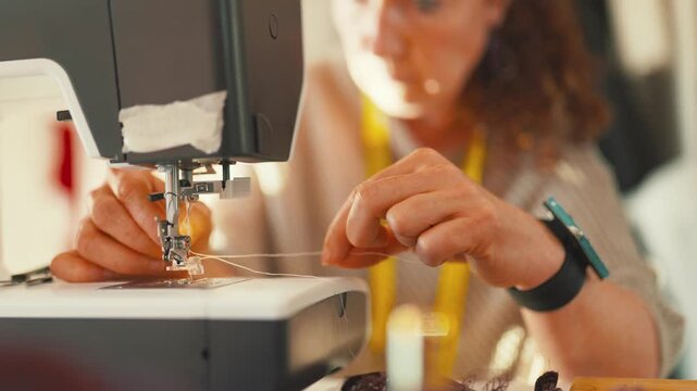 Seamstress threading sewing machine needle in atelier