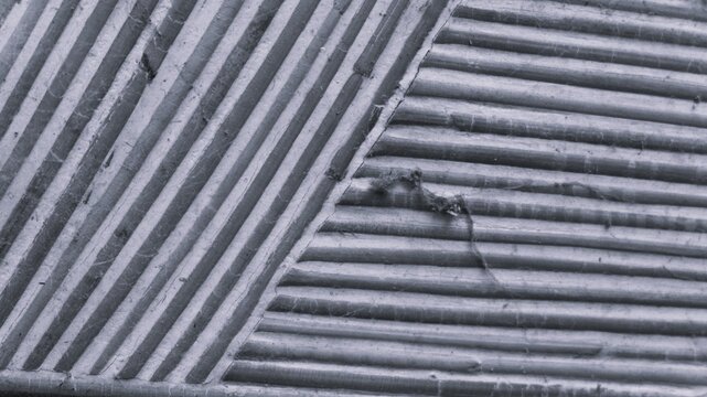 Black and white close-up of corrugated panel texture with diagonal seams, parallel ridges, dust fibers, and worn industrial surface detail.