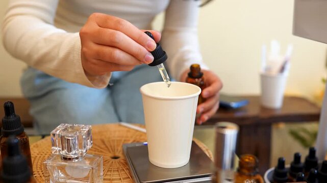 Hands carefully mixing essential oils in a preparation cup surrounded by aromatherapy supplies. Natural skincare production, herbal wellness, cosmetic formulation and holistic lifestyle concept.
