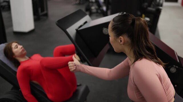 Exhausted athlete struggles through the final repetitions on a leg press machine while her trainer encourages her to keep going and finish the set strong