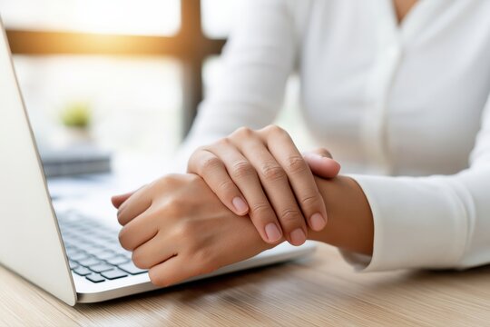 Close-up of a woman's hands holding her wrist in pain while working on a laptop computer.