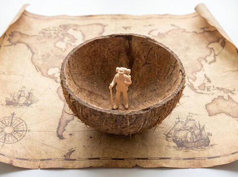 Tiny Figurine Standing in Coconut Shell on Vintage World Map as Narrow Worldview Metaphor