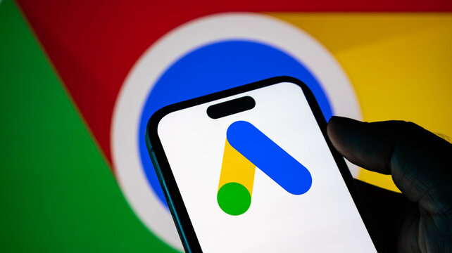 Closeup of a smartphone displaying the google ads logo with the google chrome browser icon in the background