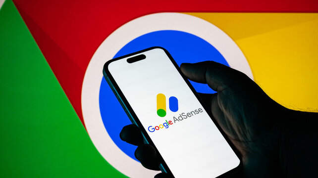 Closeup of a hand holding a smartphone displaying the google adsense logo against a google chrome background