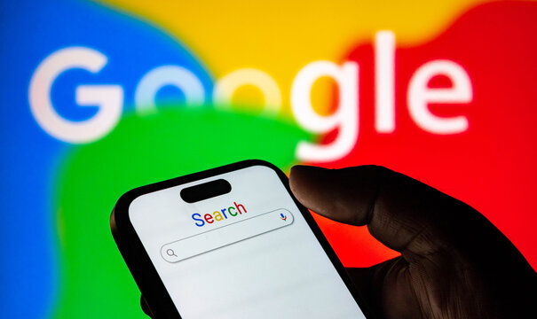 Closeup of a hand holding a smartphone displaying the google search bar against a colorful google logo background