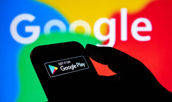 Closeup of a hand holding a smartphone displaying the google play store logo against a colorful google background