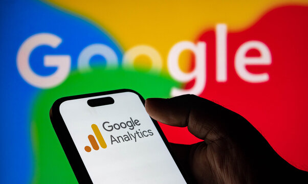 Closeup of a hand holding a smartphone displaying the google analytics logo with the google logo in the background
