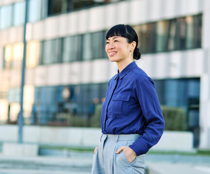Portrait of a young asian japanese businesswoman woman walking down the street, surrounded by moder corporate office buildings