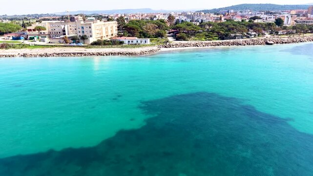 Aerial view of Maria Pia Beach seen from the sea showing turquoise water sandy coastline and Mediterranean shoreline in summer light.