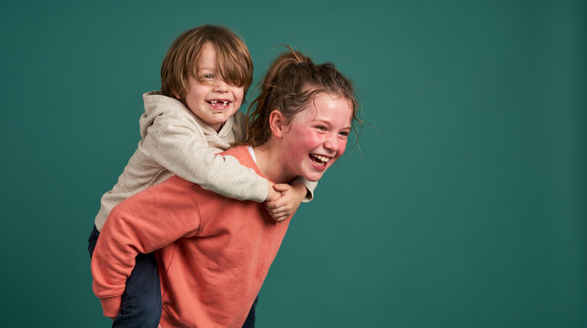 Happy Sister Giving Brother Piggyback Ride on Teal Background