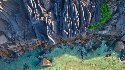 Stunning drone top-down view of the famous massive sculpted granite boulders at Anse Grosse Roche, crashing waves, and crystal clear turquoise ocean water in La Digue, Seychelles. © Nils