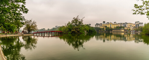 Fototapeta premium A panorama view across the north side of the Hoan Kiem Lake towards the Huc Bridge and the Ngoc Son Temple in Hanoi, Vietnam, in the morning