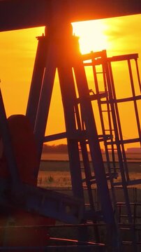 Silhouette of oil pump jack against a colorful beautiful sky with glowing clouds at sunset